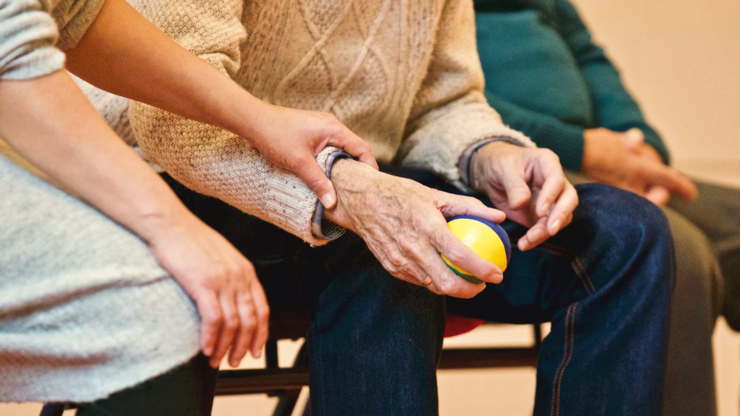 a senior's hand holding a stress ball with the care person's hand holding their wrist