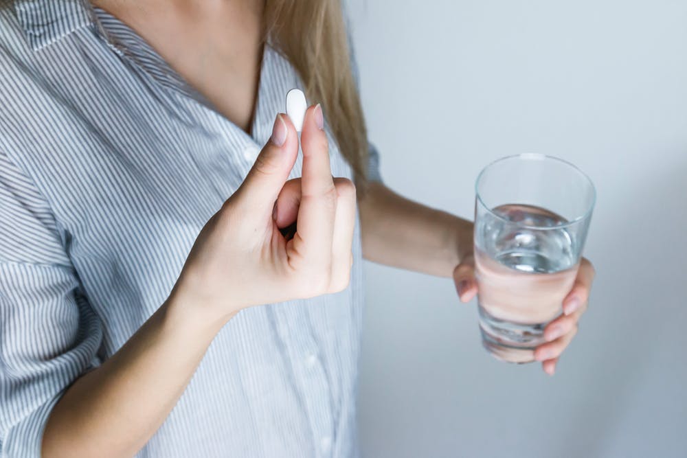 a hand holding a pill with the other hand holding a glass of water