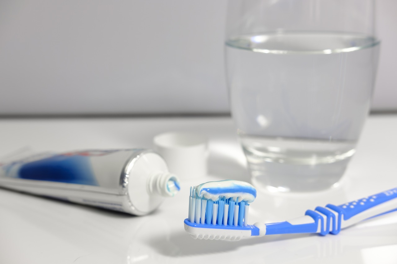 a toothbrush with toothpaste on the bristles in the foreground, and a opened bottle of toothpaste and a glass of water are in the background