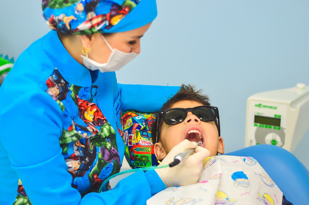 a dentist wearing a brightly coloured scrub uniform cleaning a child's teeth