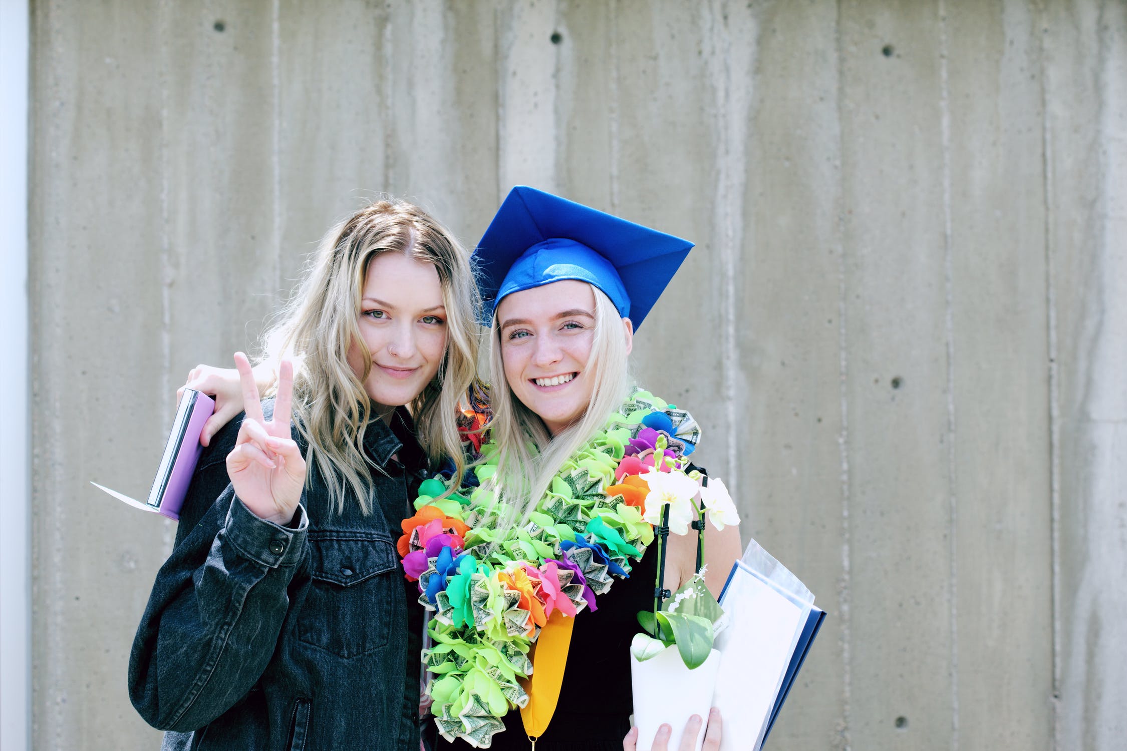 two smiling friends, one with a graduation cap on