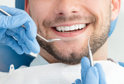 A close-up of a man smiling, with dental tools held in front of his teeth.