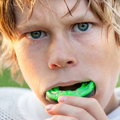 A young kid putting a green mouthguard in his mouth