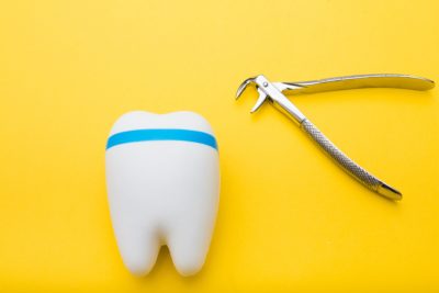 A 3d tooth on a yellow background next to a silver dental tool