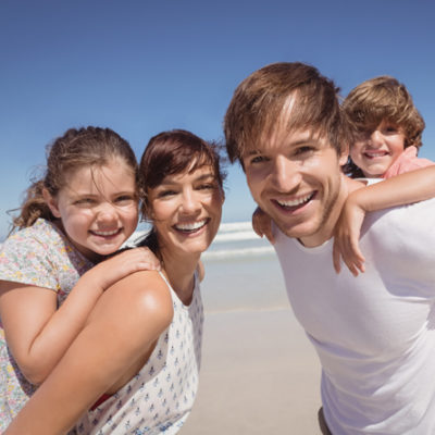 a family smiling on the beach with the ocean behind them