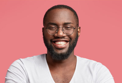 A black man wearing glasses gives a big smile.