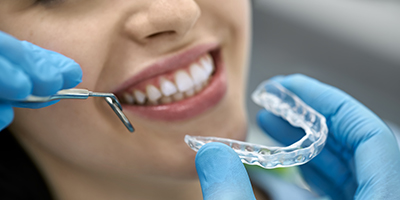 A woman smiles as a dentist holds a nightguard in front of her mouth