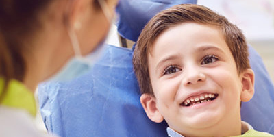 A white child sits in a dentist chair and smiles at a dentist