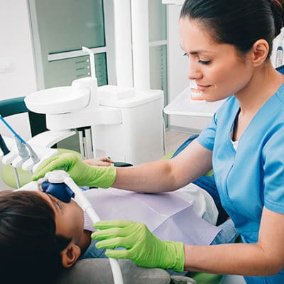 A dentist places a machine over a patient's nose to sedate them during a procedure