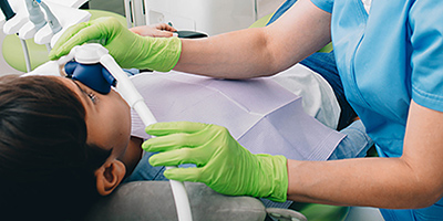 A dentist wearing green gloves places a sedation machine over a patients nose